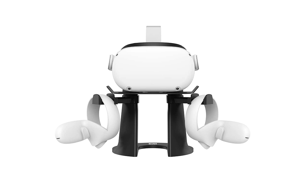 A black stand holding a white virtual reality headset and two controllers, designed for models like the Oculus Quest 2 or HTC Vive. The stand securely supports the headset on top with the controllers mounted on either side.